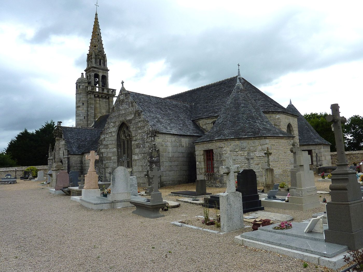 L'église Saint-Pierre de Berrien, en granite, avec son clocher et les tombes du vieux cimetière