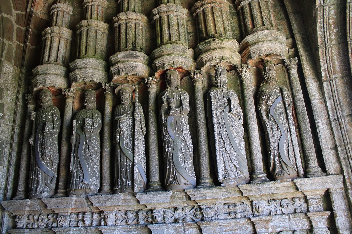 Statues d'apôtres en pierre sous le porche sud de l'église Notre-Dame de Bodilis, au-dessus d'une frise sculptée