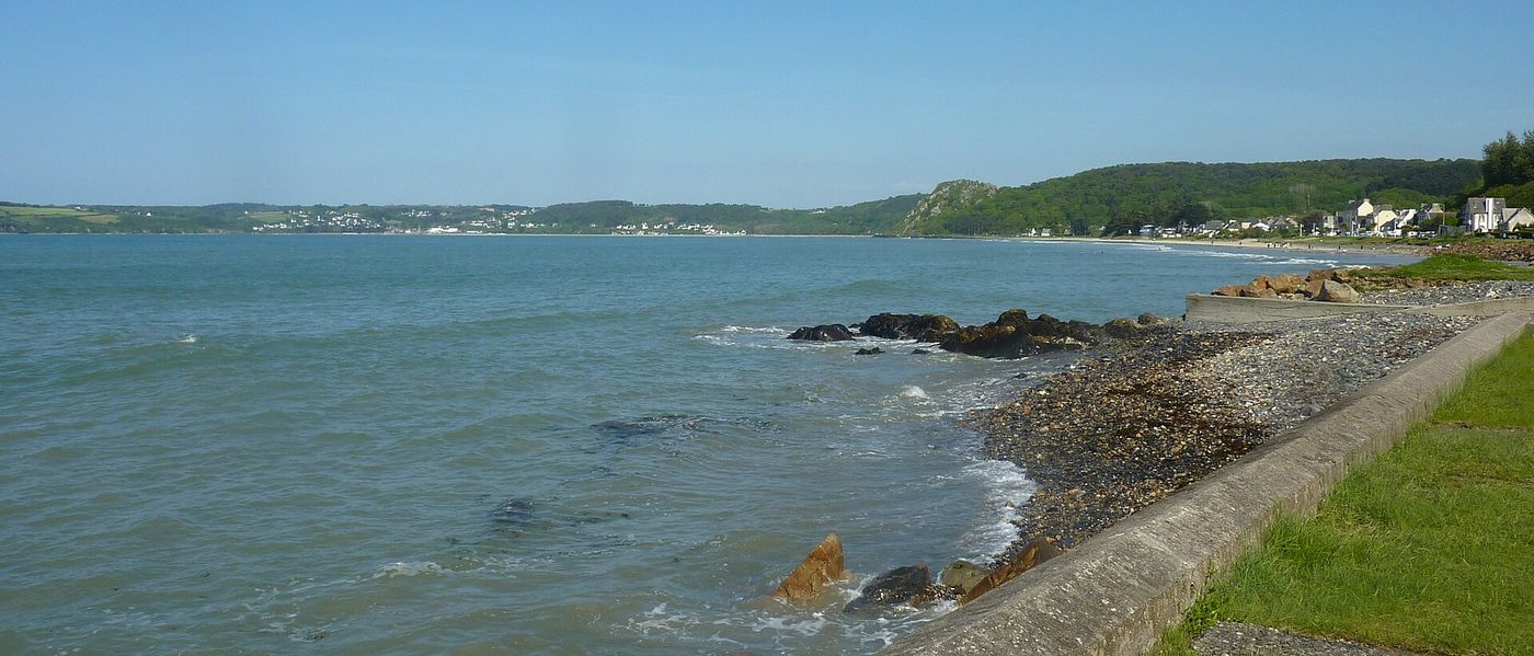 Vue sur la Lieue de Grève à Plestin-les-Grèves : la mer, une digue de pierre et la côte boisée au loin