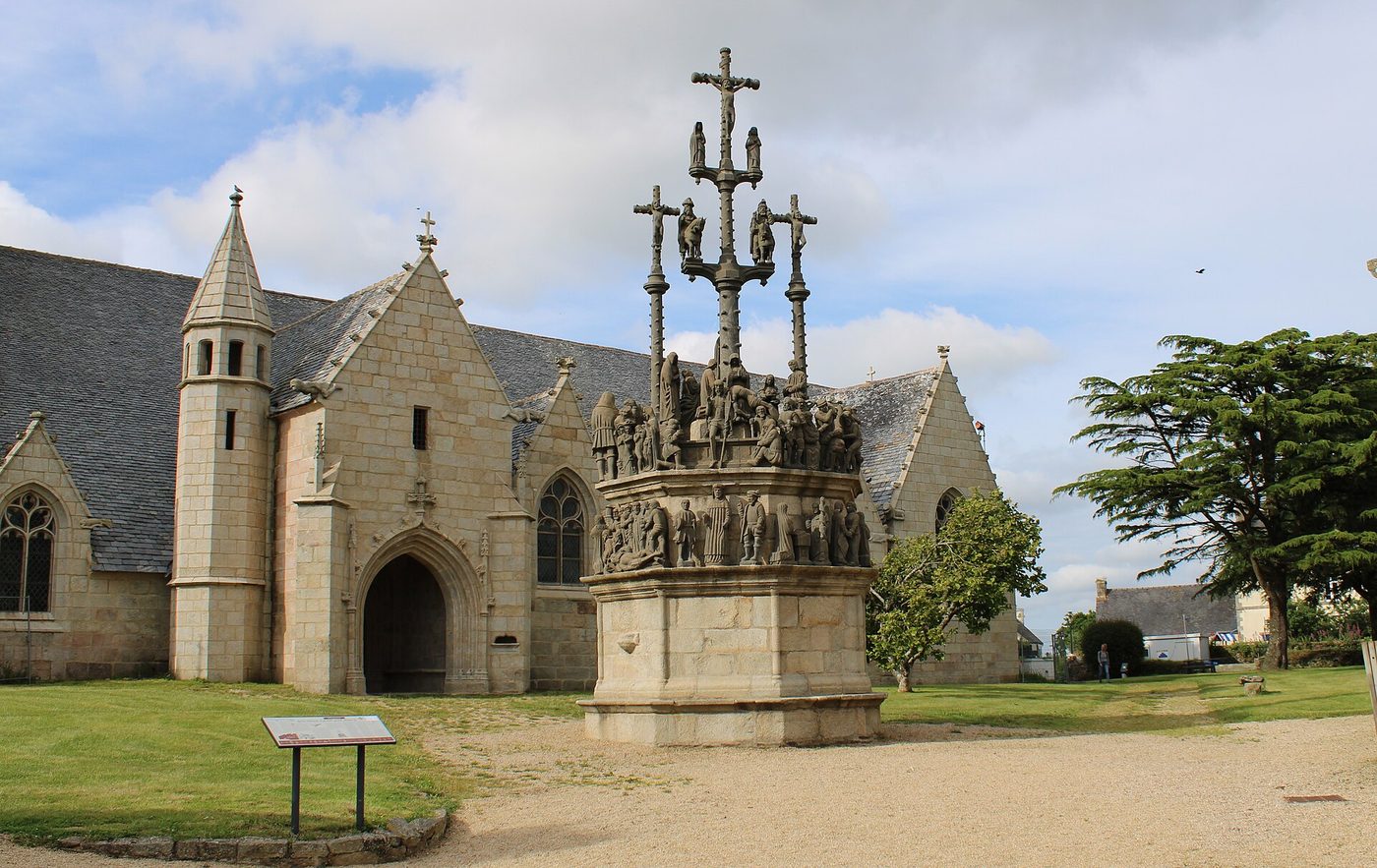 Calvaire de pierre aux nombreux personnages sculptés devant l'église Saint-Yves de Plougonven, sous un ciel nuageux